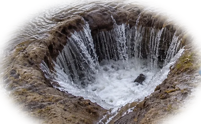 A muddy sinkhole with lake water pouring into it